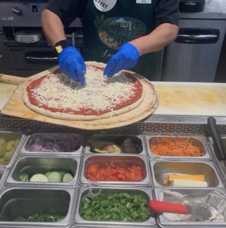 Photo: Down to Earth deli team member making a pizza fresh from scratch