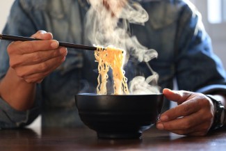 Photo: A man holding chopsticks with ramen noodles over a steaming bowl