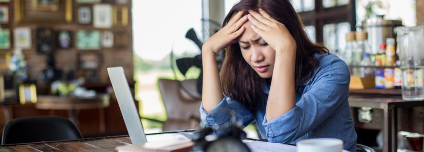 Photo: Woman holding her head and using a laptop